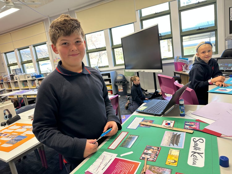 A student working in a bright classroom on a project for the CWA Country of Study poster.